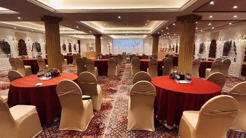 An image of a banquet hall in Mahabalipuram with round tables, chairs, carpeted floors, and a projector - Kaldan Samudra Palace, one of the Best Wedding Venues in ECR.